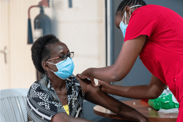 Amref staff vaccinating an elderly African women