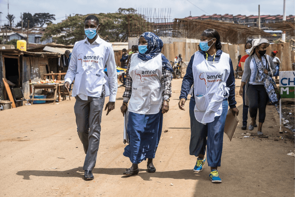 Amref community health workers walking in the community with masks and other branded aprons on