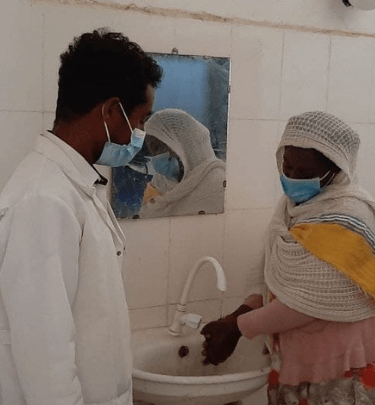 Two Ethiopians both with masks on with one washing their hands
